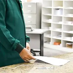Pessoa com jaleco verde segurando documento sobre balc&atilde;o em ambiente de trabalho