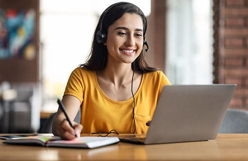 Uma mulher usando notebook e com headseat na cabeça. Cursos na modalidade Digital (EAD)